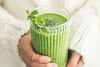 Hands with gold ring holding matcha smoothie with chia seeds and mint leaves